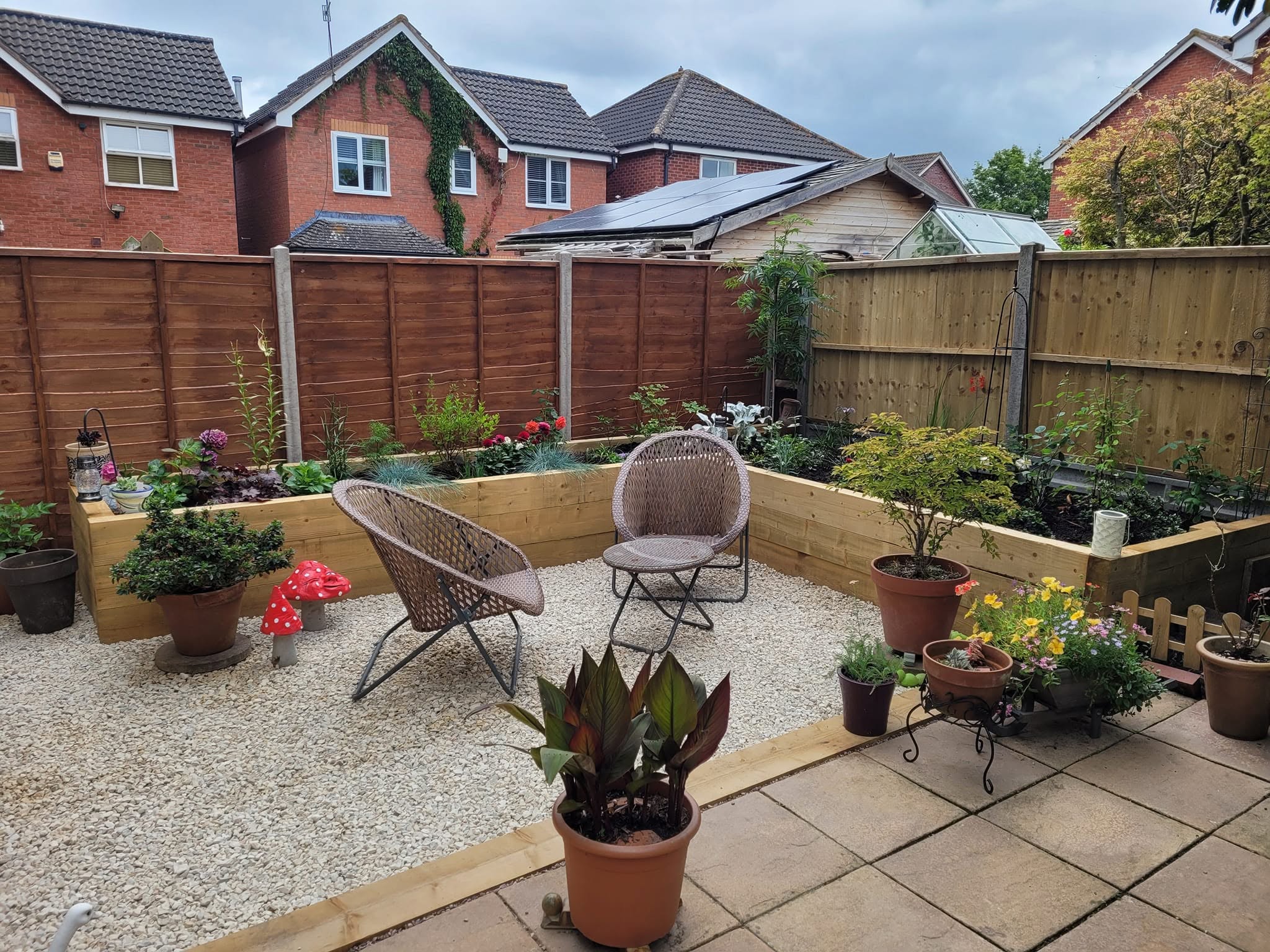Gravel seating area with chairs, raised sleeper beds and pots in a finished garden